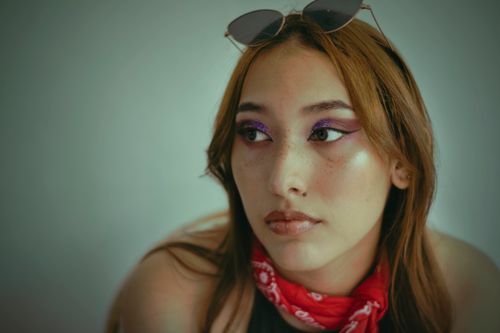Free Portrait of a young woman with sunglasses, stylish makeup, and a red scarf, looking thoughtful. Stock Photo