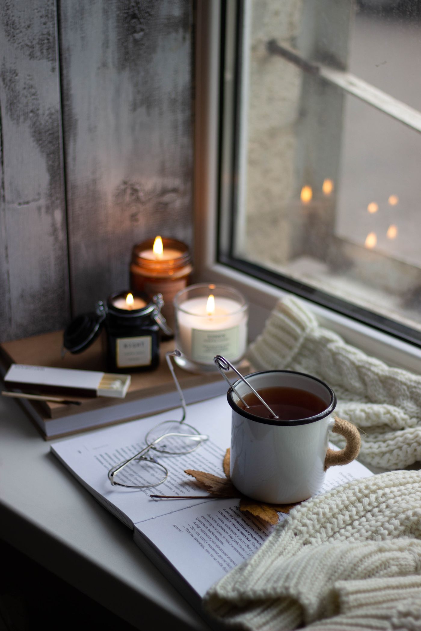 Candles, a book and a cup of tea on a windowsill