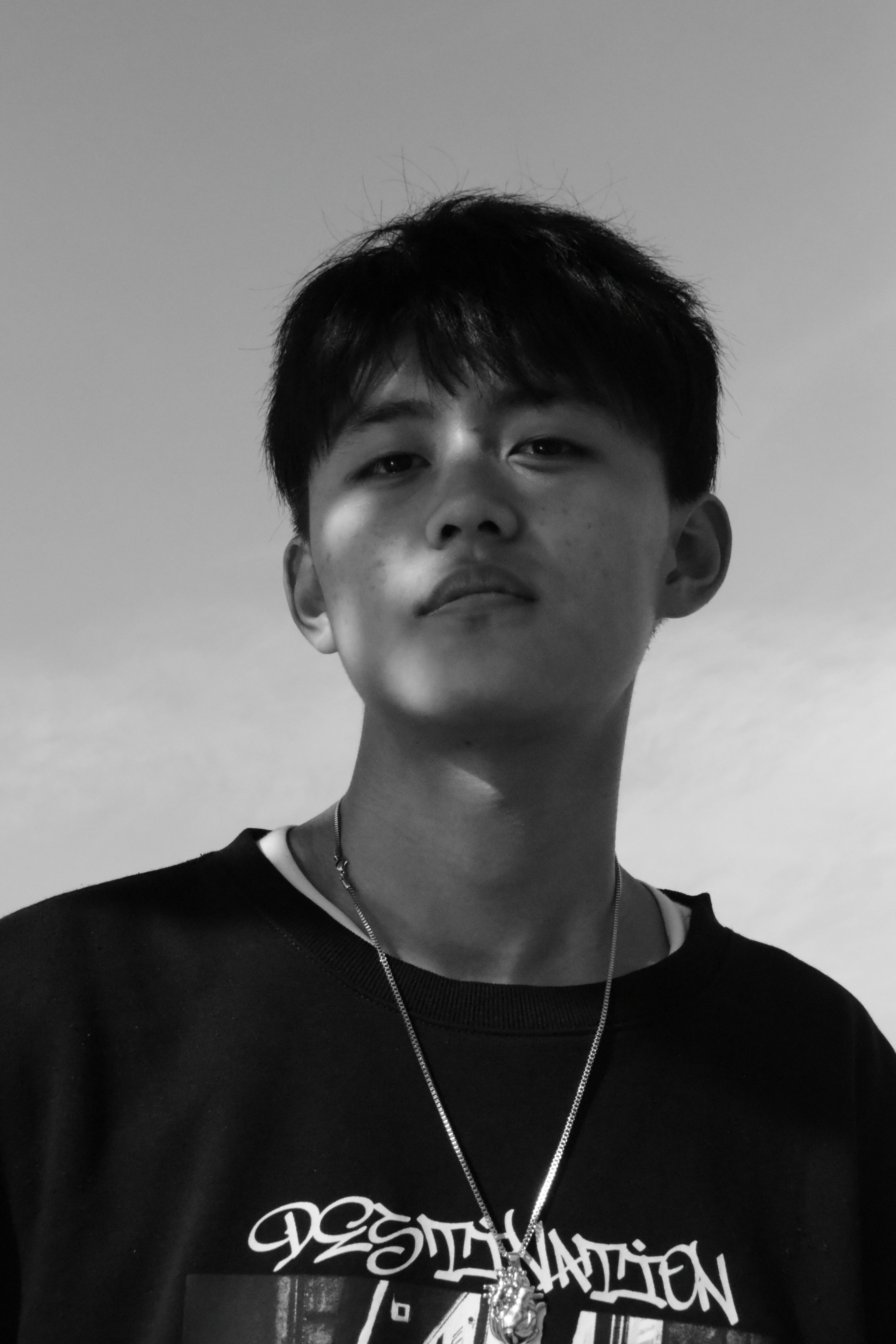 Black and white portrait of a young man wearing a necklace, showcasing expressive features.