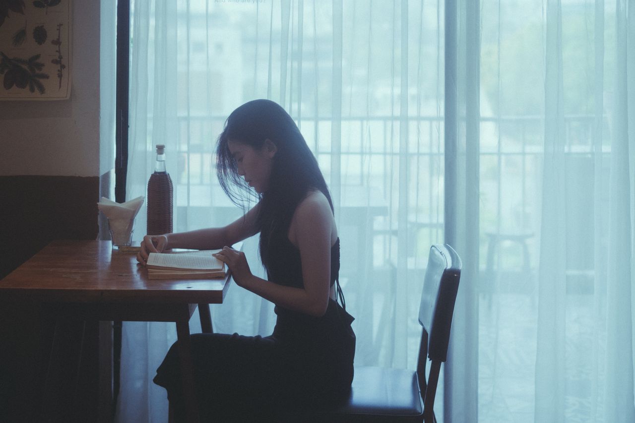 a woman engrossed in a book at a cafe table with gentle lighting throu