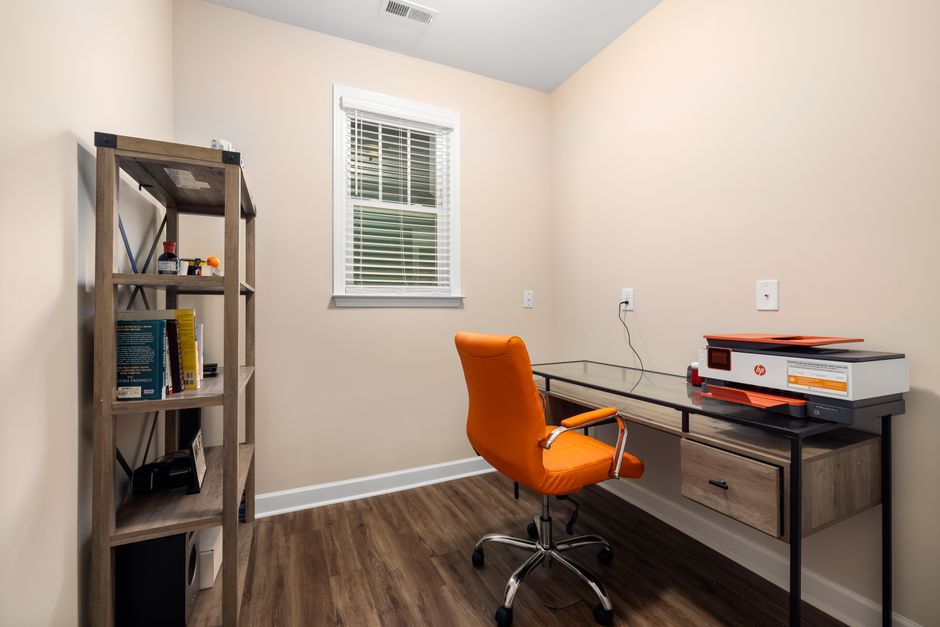 A clean and organized home office featuring a glass desk and vibrant orange chair.