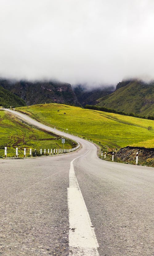 Gray Concrete Road Between Green Grass Field