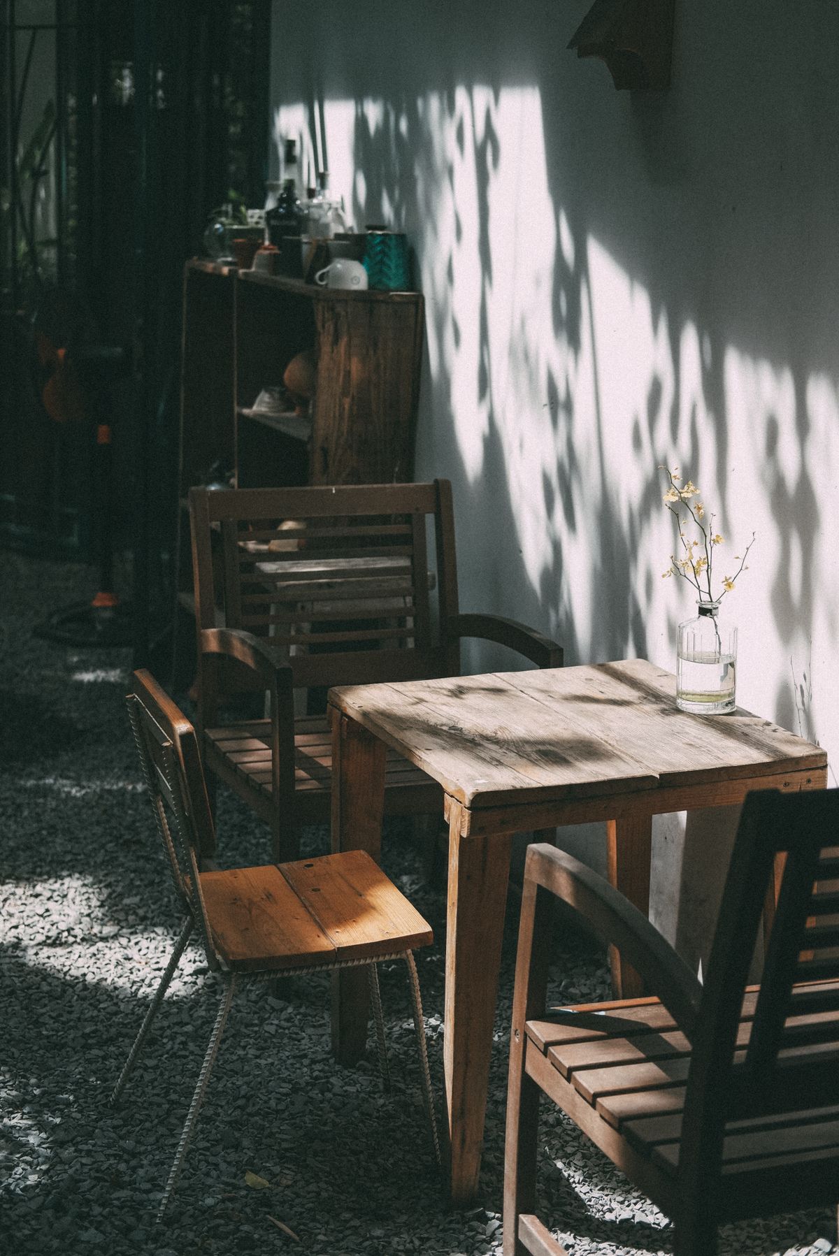 A sunlit outdoor patio features rustic wooden chairs and a table against a textured wall, creating a serene atmosphere. Stock Photo.