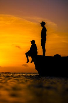 Silhouettes of two people on a boat during a vibrant sunset over the ocean.