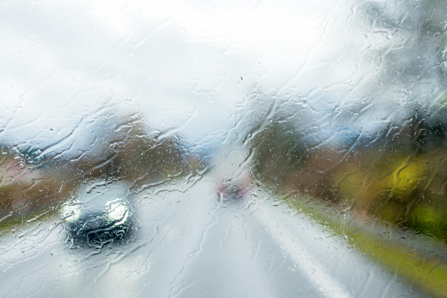 A car seen through a rain-soaked windshield, depicting a rainy day drive.