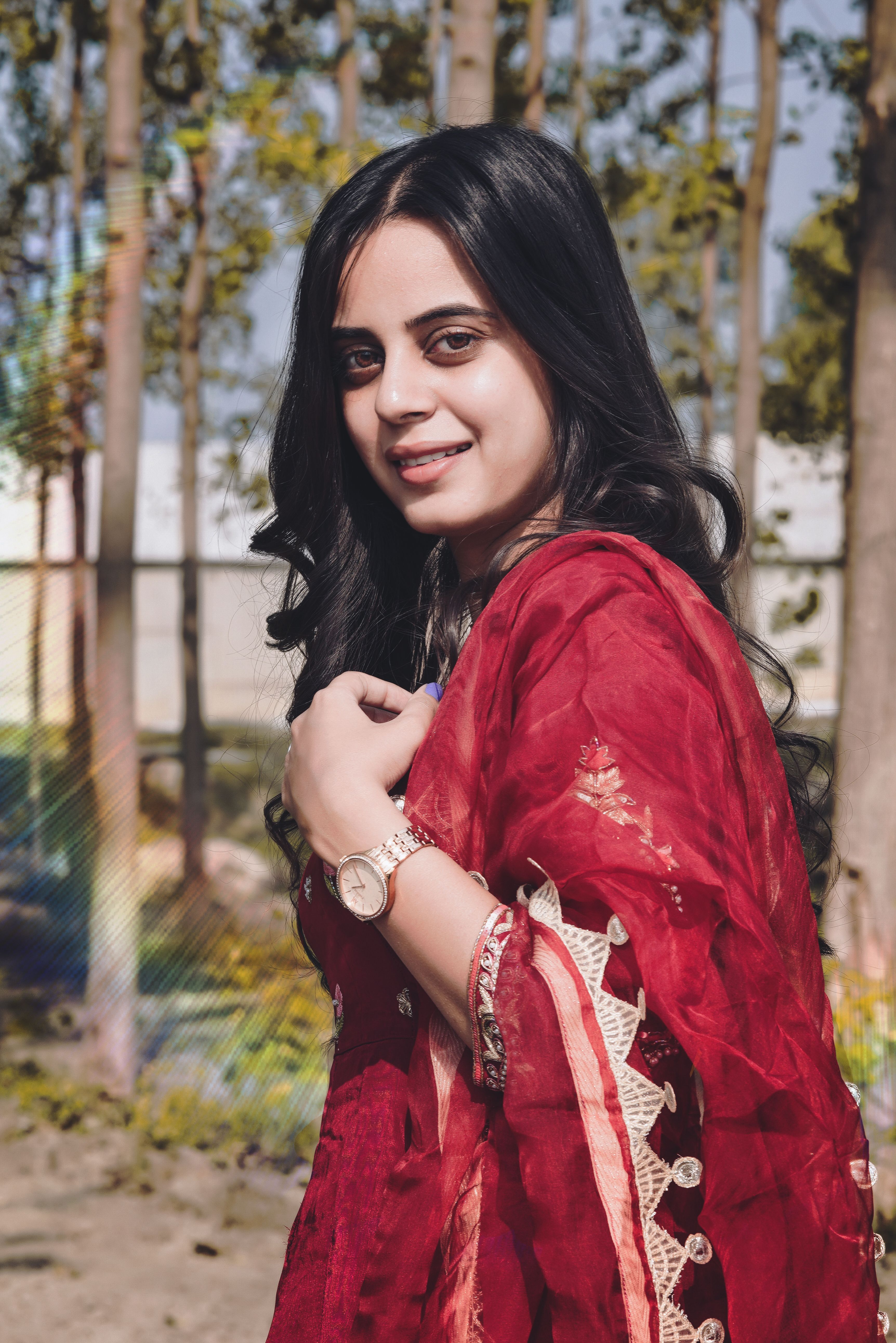 Portrait of a young woman in a traditional red sari smiling outdoors on a sunny day.