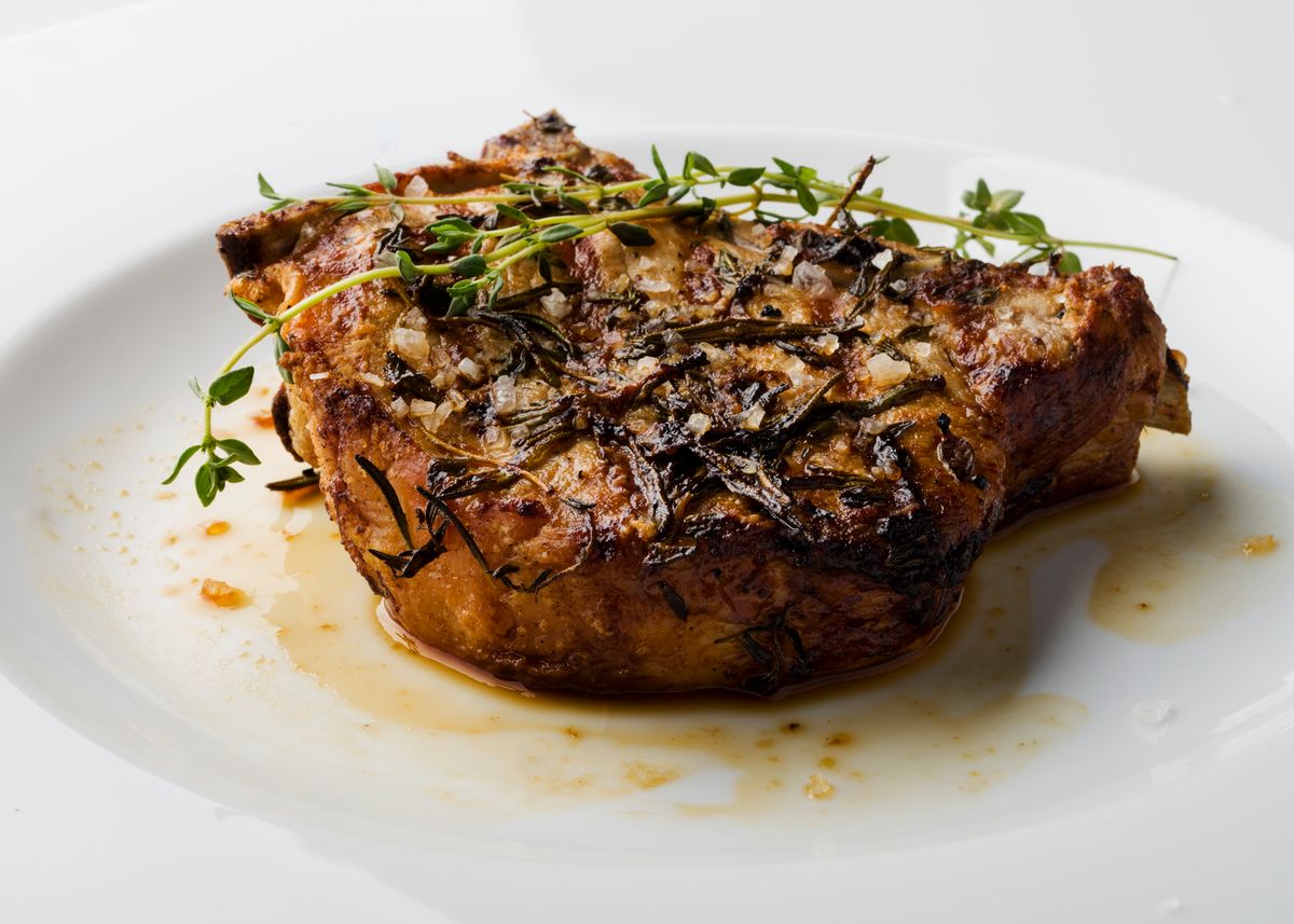 Thick seared bone-in pork chop with thyme sprigs and pan juices on a white plate