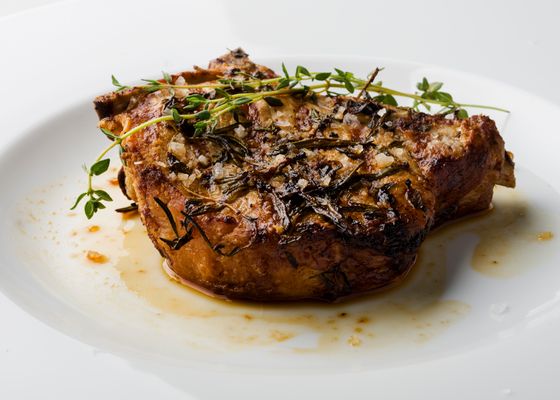 Thick seared bone-in pork chop with thyme sprigs and pan juices on a white plate