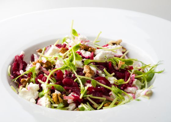 Shredded roasted beets with crumbled goat cheese, walnuts and pea shoots in white bowl