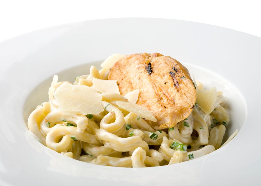 A bowl of wide egg noodles and shredded chicken in a thick, glossy gravy, topped with a scattering of black pepper and chopped parsley.