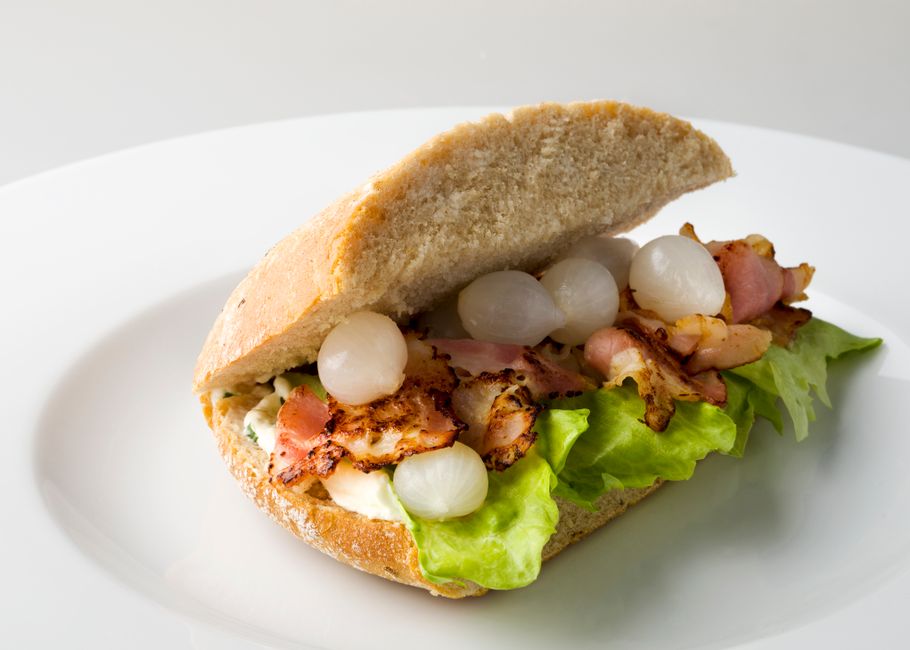 A BLT sandwich cut diagonally on a plate, showing layers of crisp bacon, lettuce, and thick tomato slices between toasted bread spread with mayo.