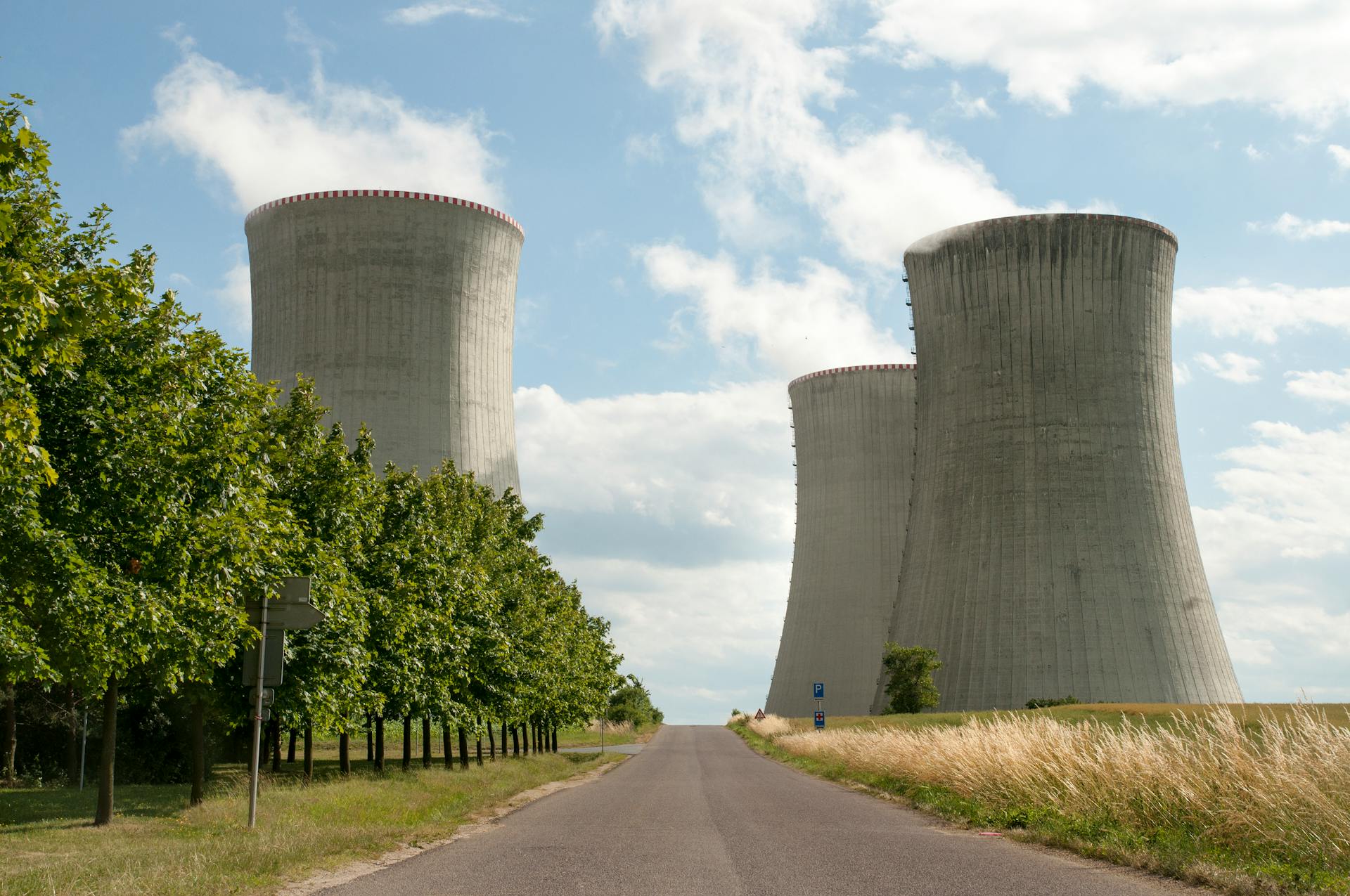 A nuclear power plant cooling towers by a road with green trees under a clear sky.