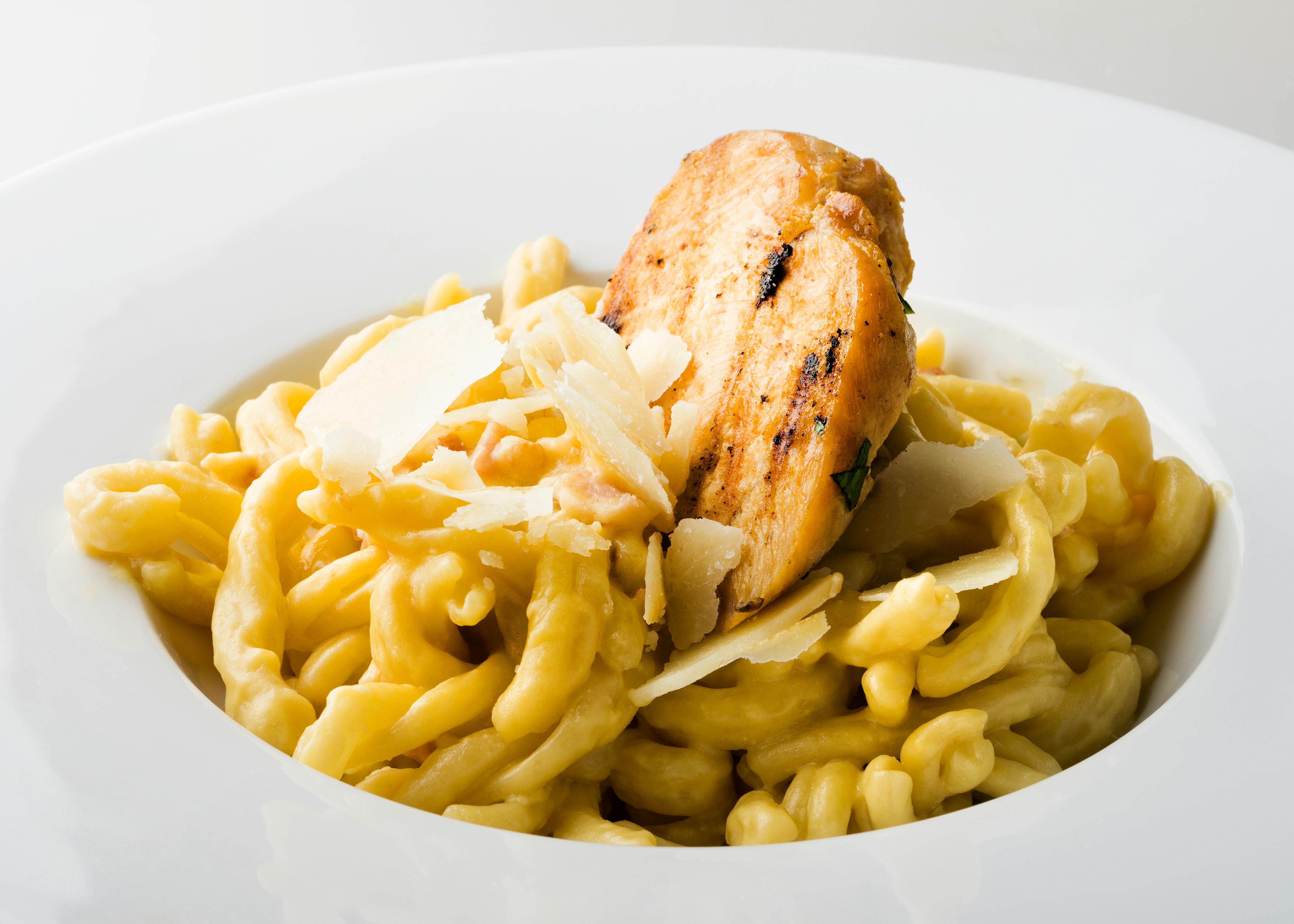 Delicious creamy chicken pasta topped with Parmesan cheese, plated elegantly in white bowl.