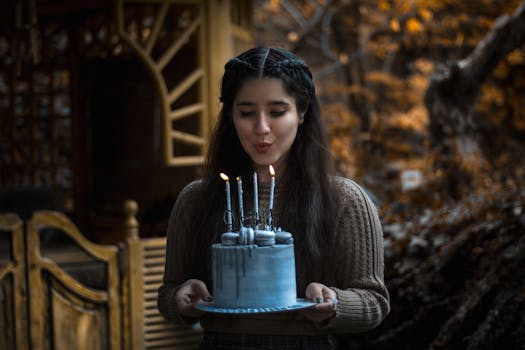 Girl celebrating birthday outdoors, blowing candles on a blue cake in an autumn setting.