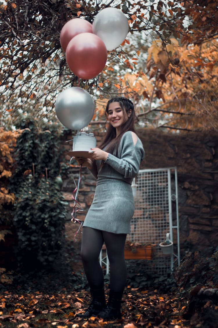 A Woman Holding Balloons And A Cake