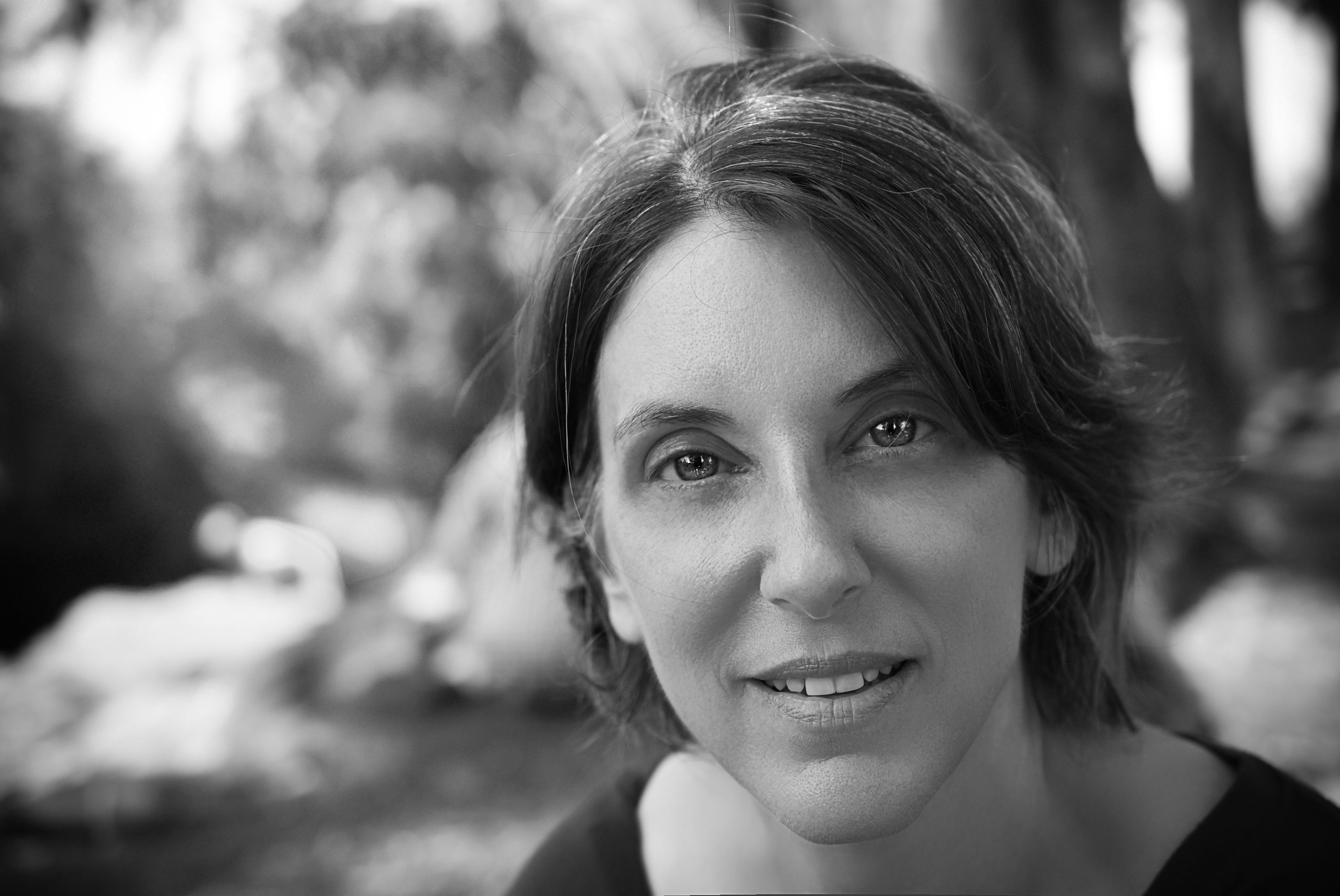 Close-up grayscale portrait of a smiling woman in a natural outdoor setting.