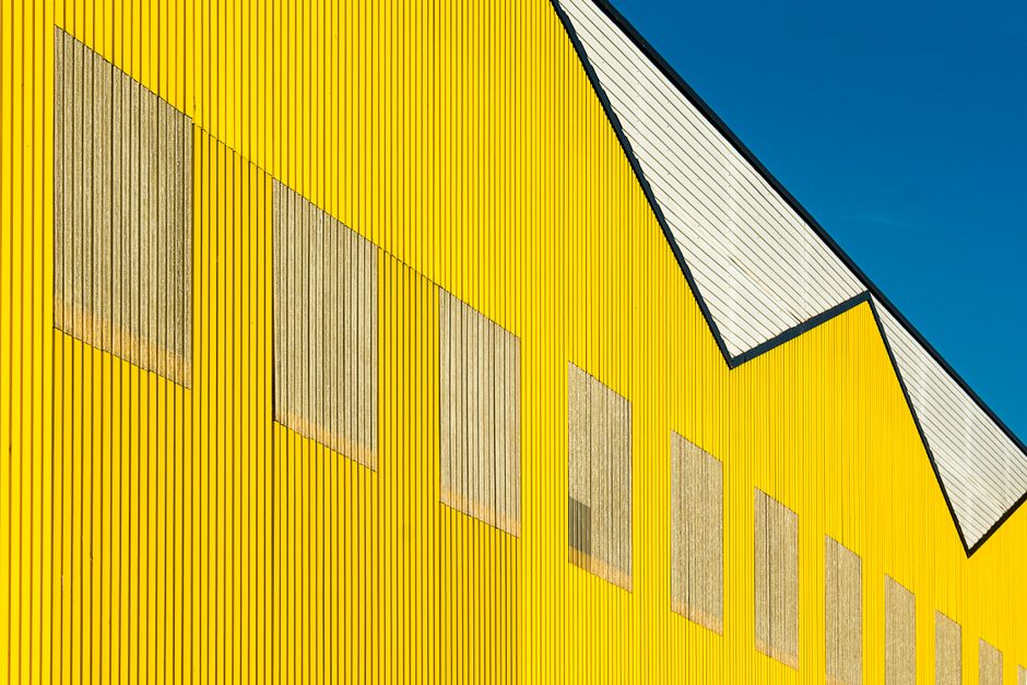 Close-up shot of a geometric yellow industrial building with clear blue sky.