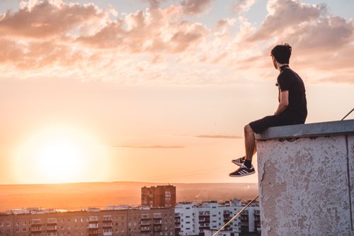 Free A young man sitting on a rooftop in Ufa, Russia, watching a vibrant sunset. Stock Photo