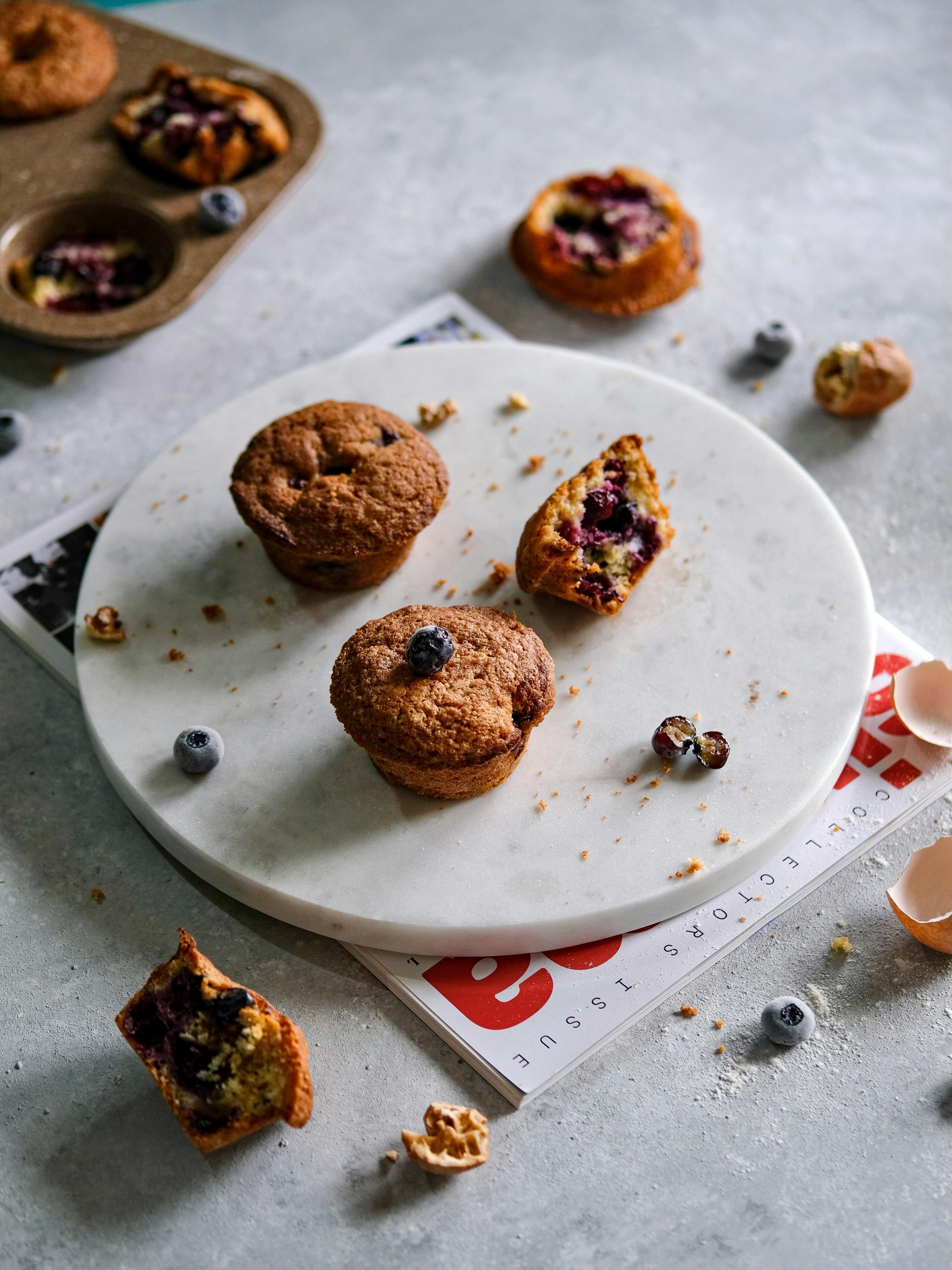 Freshly baked blueberry muffins displayed elegantly on a marble plate with scattered blueberries.