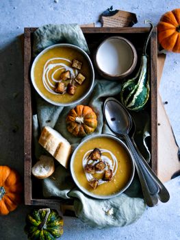 Warm and inviting fall-themed pumpkin soup served with croutons, showcased with gourds and bread in a wooden tray.