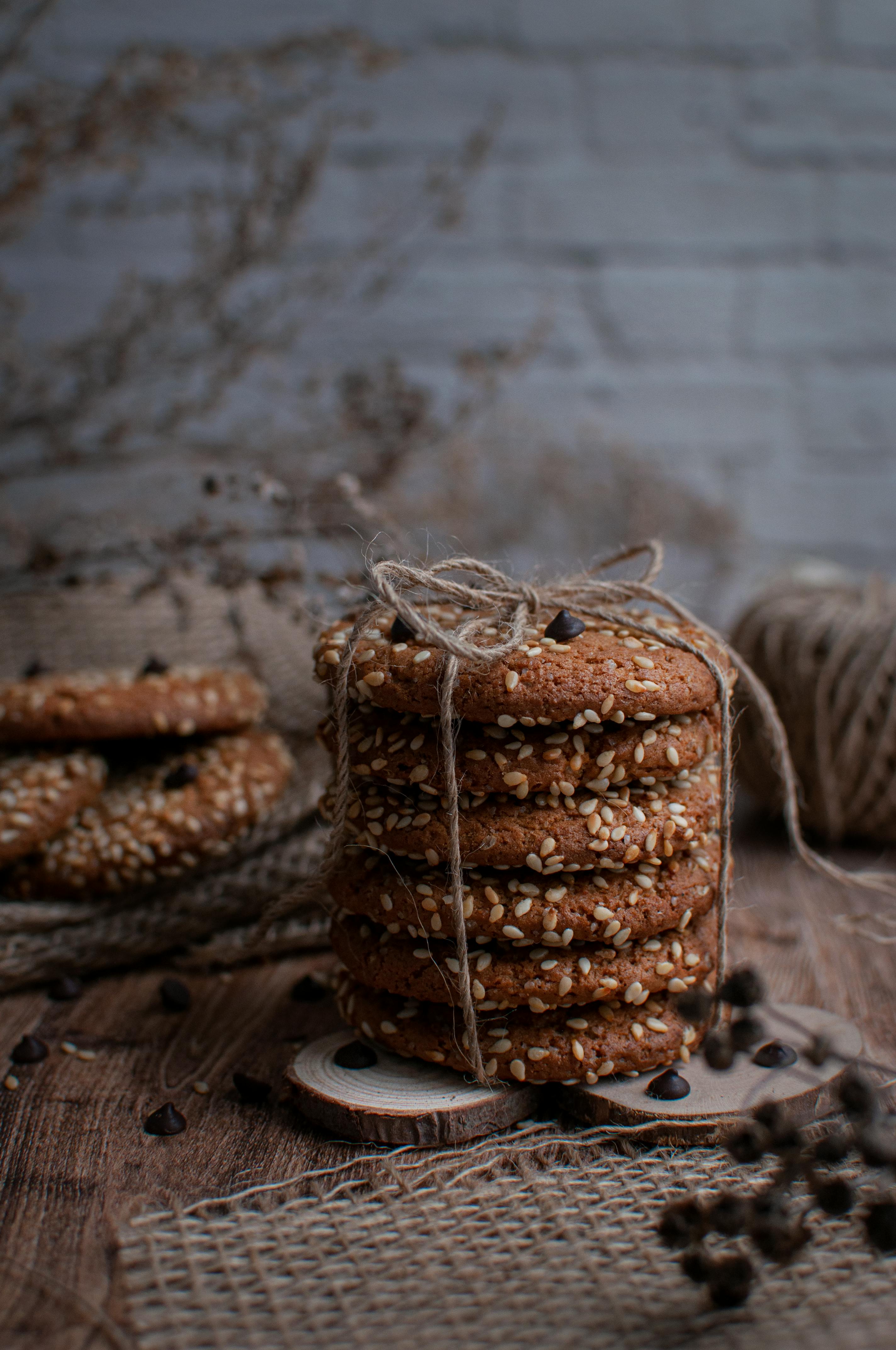 Stack of homemade chocolate chip cookies with sesame seeds on a rustic wooden table.