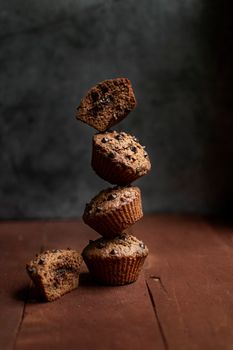 A stack of chocolate chip muffins balancing on a wooden surface with a moody backdrop.