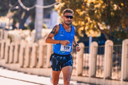 Free Focused male athlete running in a street marathon under bright sunlight. Stock Photo