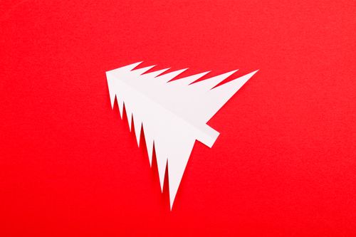 Free Simple white paper Christmas tree illustration on a vibrant red background, perfect for holiday themes. Stock Photo