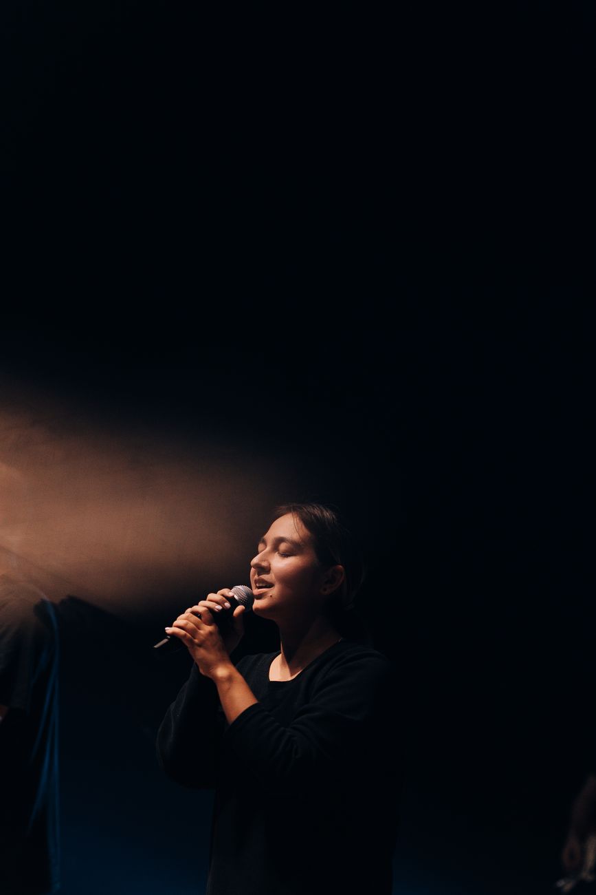 Een vrouwelijke zangeres voert gepassioneerd op het podium uit onder een dramatisch spotlicht.
