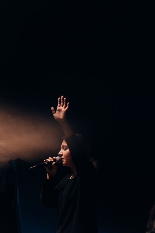 Free A woman sings with passion, eyes closed and arm raised, captured in a dramatic stage spotlight. Stock Photo