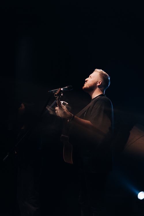 Free A male musician passionately singing and playing guitar live under dramatic lighting. Stock Photo