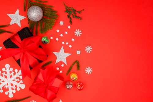 Free Christmas-themed flat lay with gift boxes, ornaments, and stars on a red background. Stock Photo