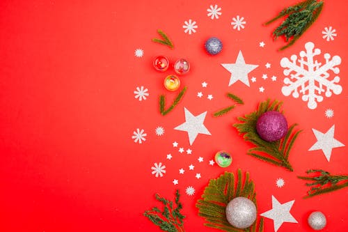 Christmas Tree Ornaments and Paper Cutouts Lying on Red Background