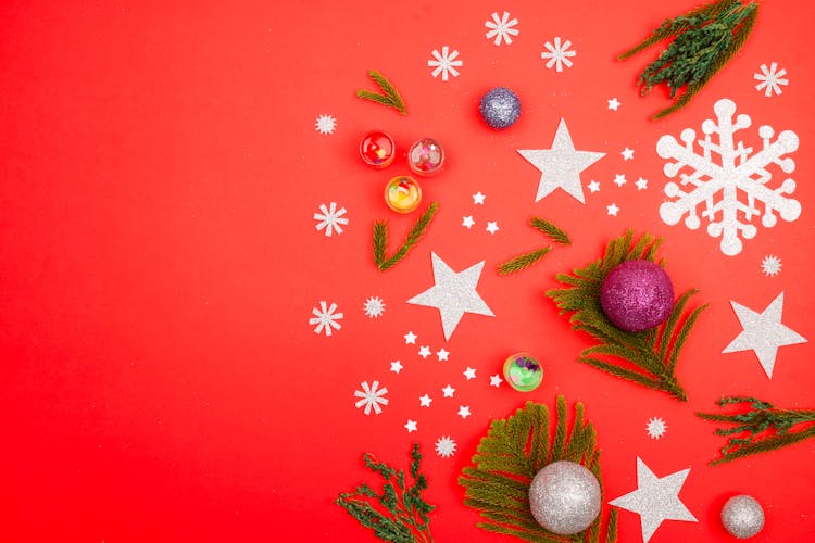 Christmas Tree Ornaments And Paper Cutouts Lying On Red Background