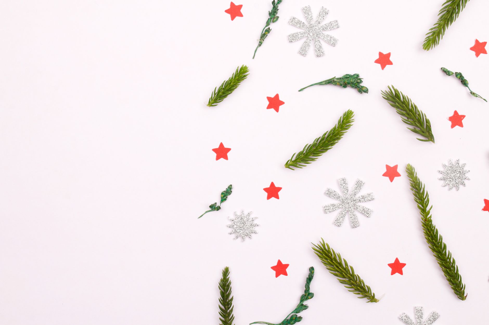 Christmas-themed flat lay with fir branches, red stars, and silver snowflakes on white background.