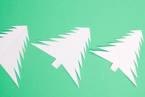 Free White paper cutout Christmas trees on a vibrant green background, showcasing minimalist holiday design. Stock Photo