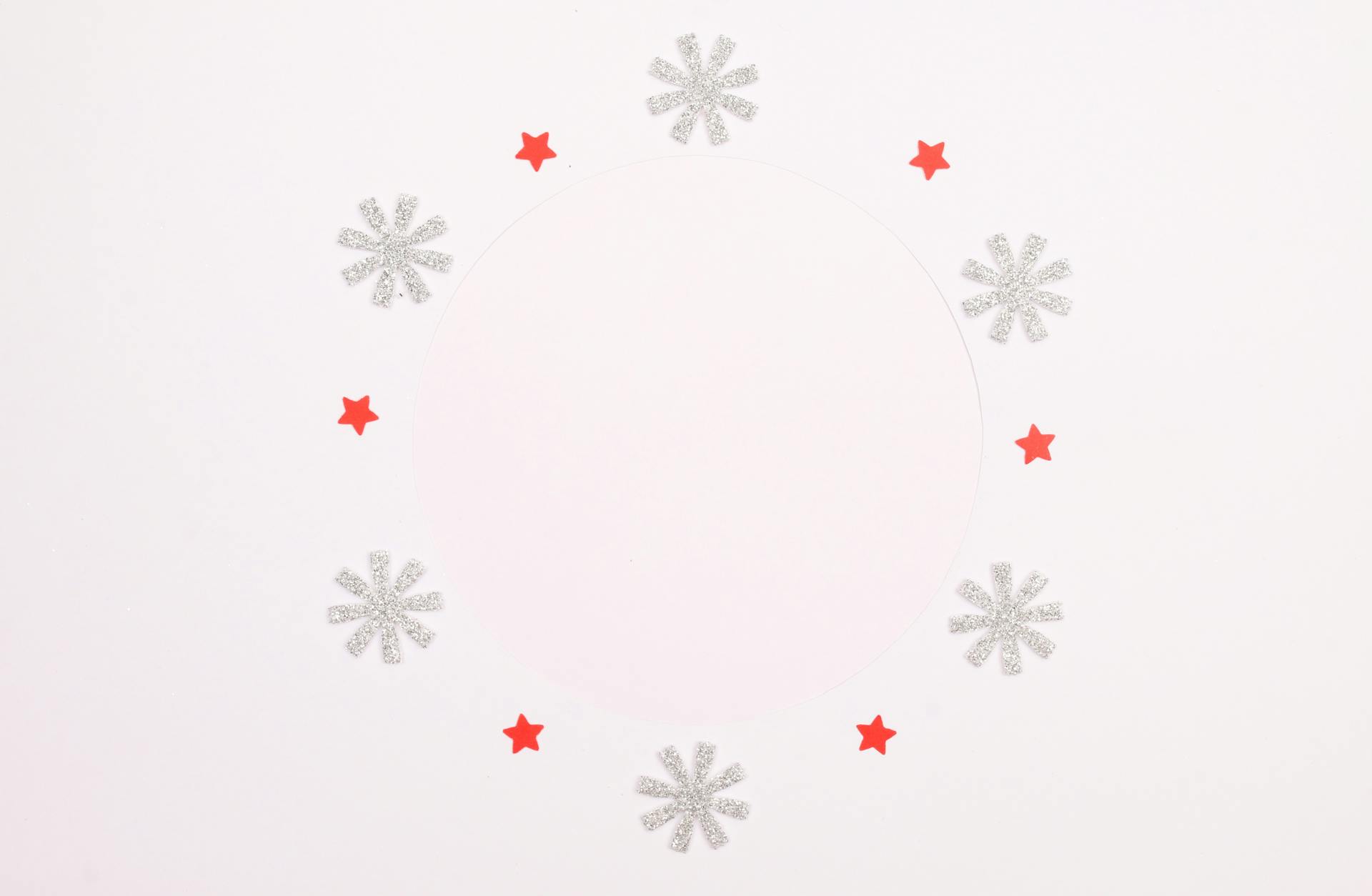 Minimalist circle design with silver snowflakes and red stars on white background.