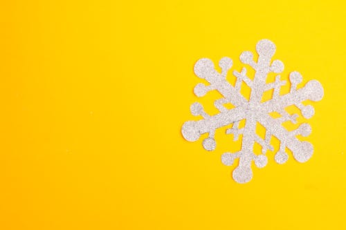 A White Snowflake Paper Cutout on Yellow Surface