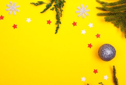Flat lay of holiday decorations with a vibrant yellow background, featuring stars and evergreen branches.