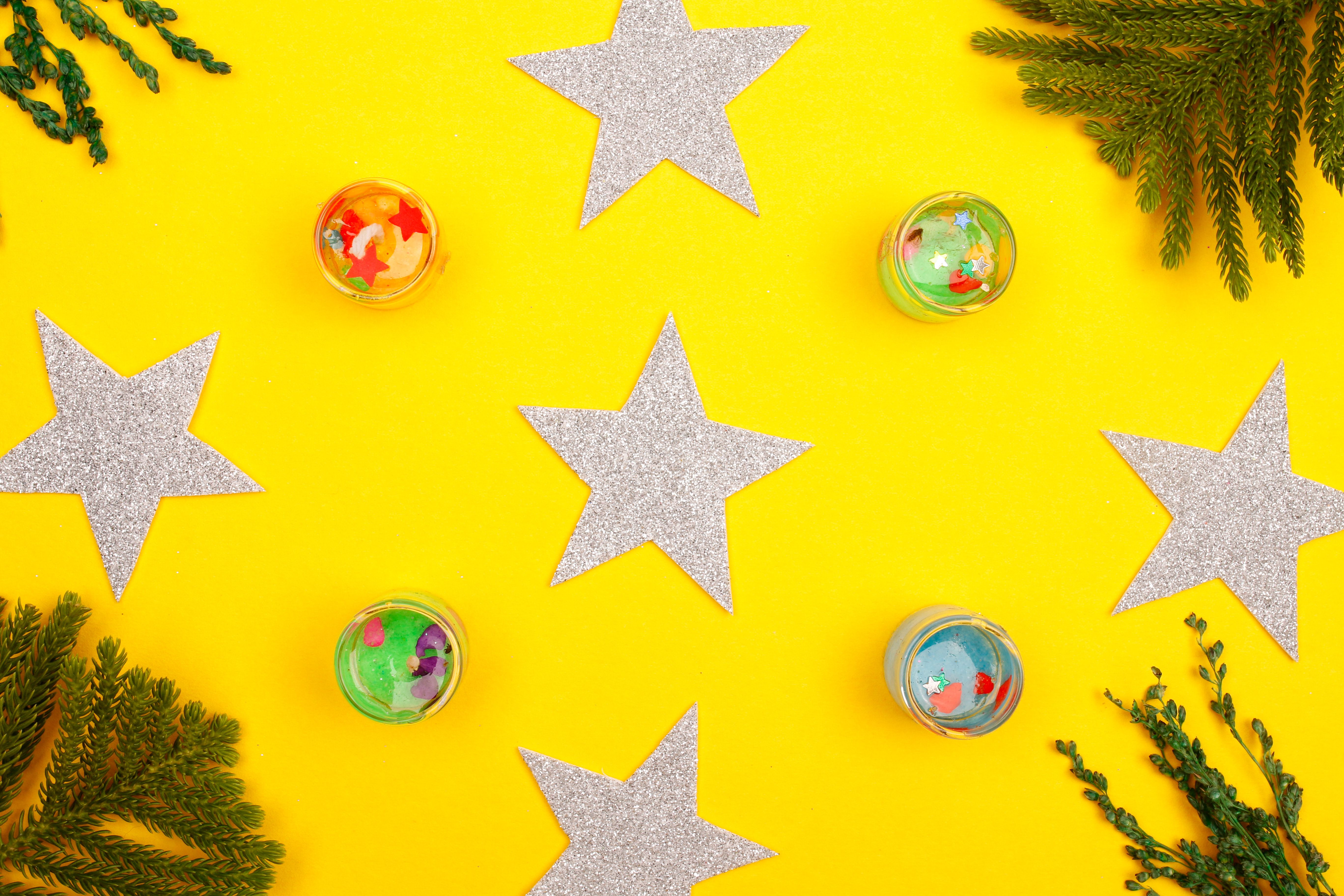 Vibrant holiday arrangement with silver stars and evergreen branches on a yellow background.