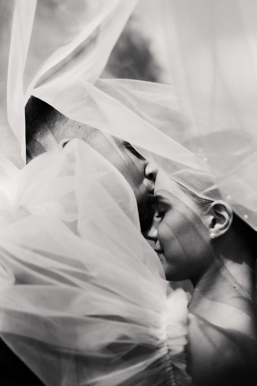 Free A romantic black and white photo of a couple sharing a tender moment under a veil. Stock Photo