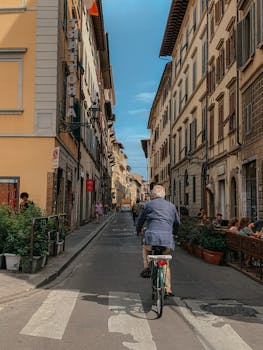 Man cycling through a picturesque urban street with historic buildings and outdoor cafes, capturing a serene moment.
