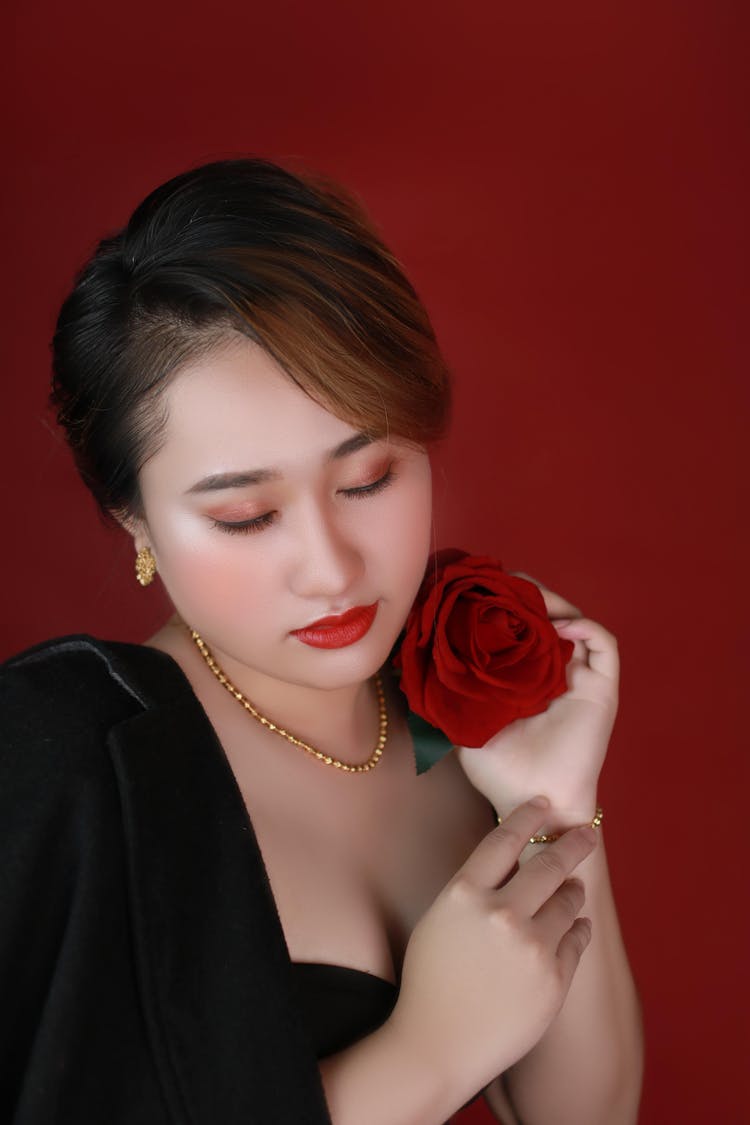 Young Beauty Wearing Classic Black Velvet Dress Holding Red Rose Close To Face