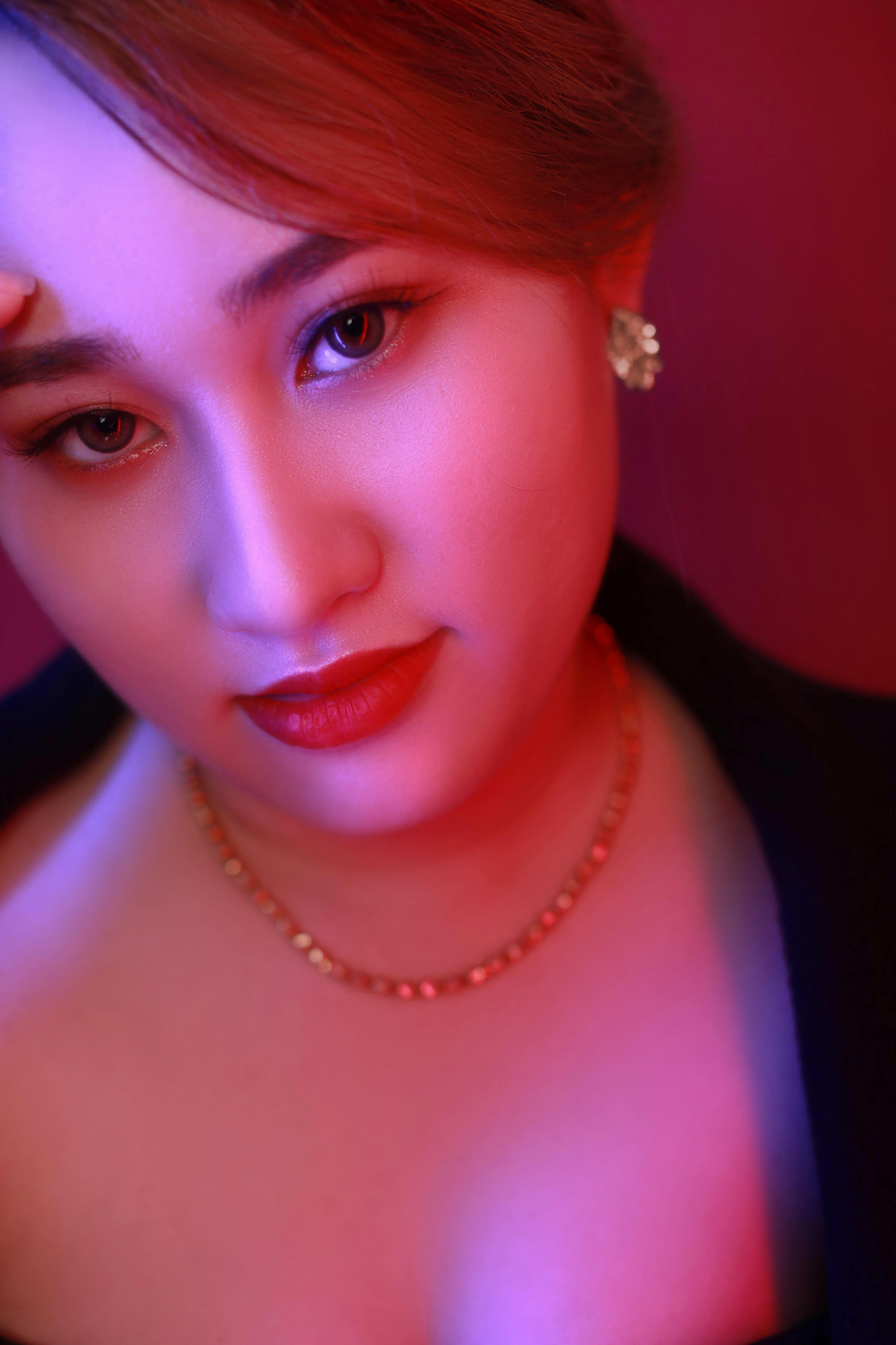 Close-up of a glamorous Asian woman with elegant makeup and jewelry in vibrant lighting.