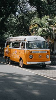 Orange vintage bus parked on a tree-lined road with summer trees in the background.