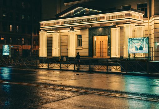 Wide-angle view of a beautifully illuminated theater entrance at night with street reflections.