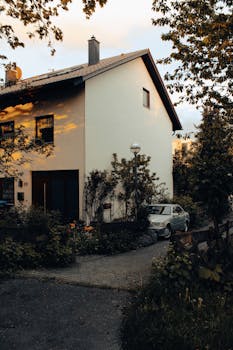 Cozy residential house with a parked car and lush garden under warm evening light.