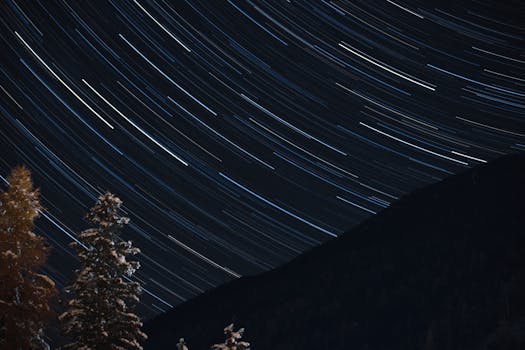 Long exposure capturing mesmerizing star trails over trees and hills at night.