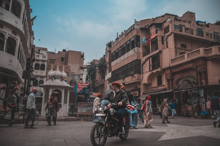 A Woman Riding A Motorbike Behind Elderly Man