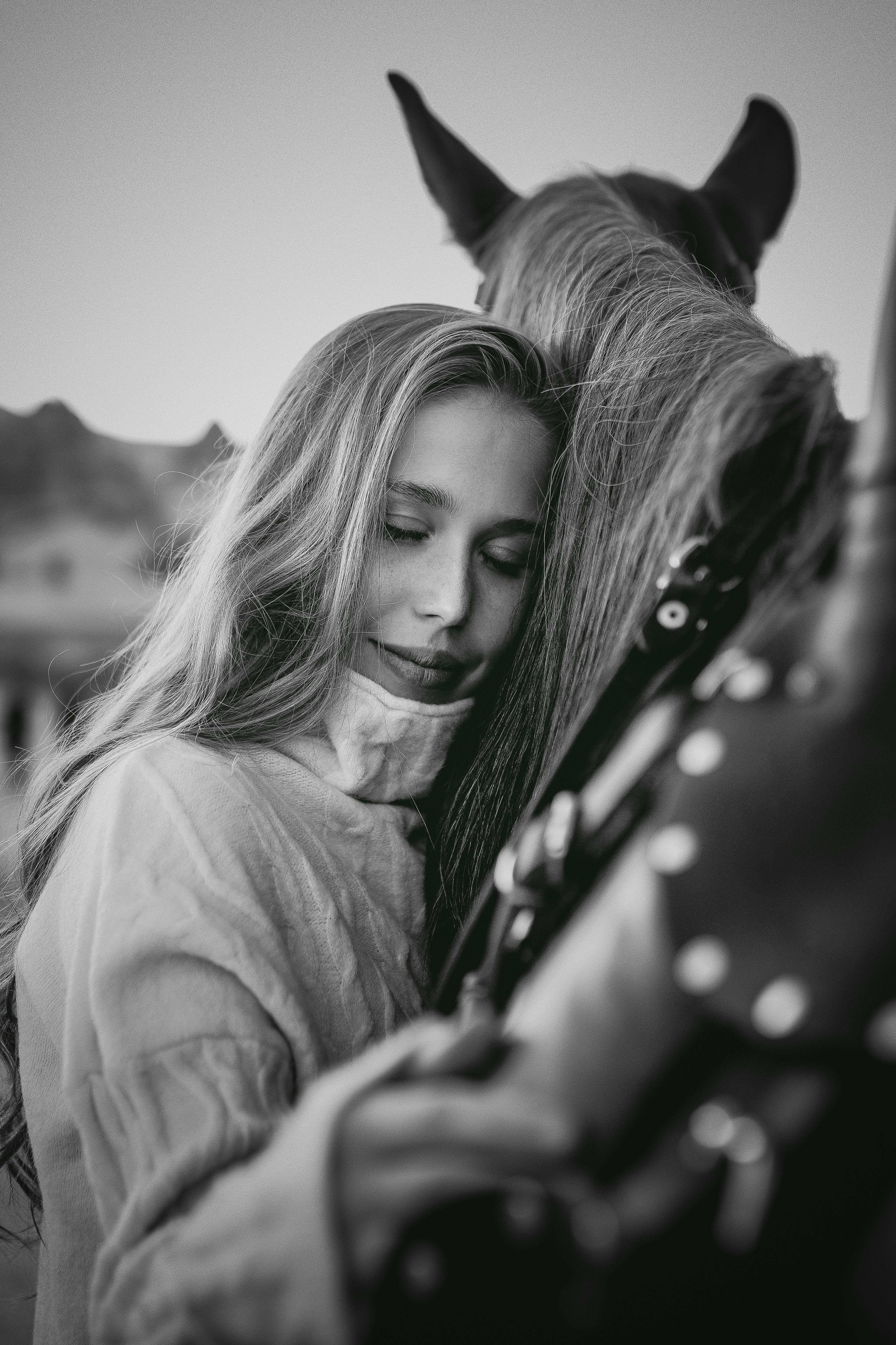 A woman lovingly hugs a horse, showcasing a bond in a serene black and white scene.